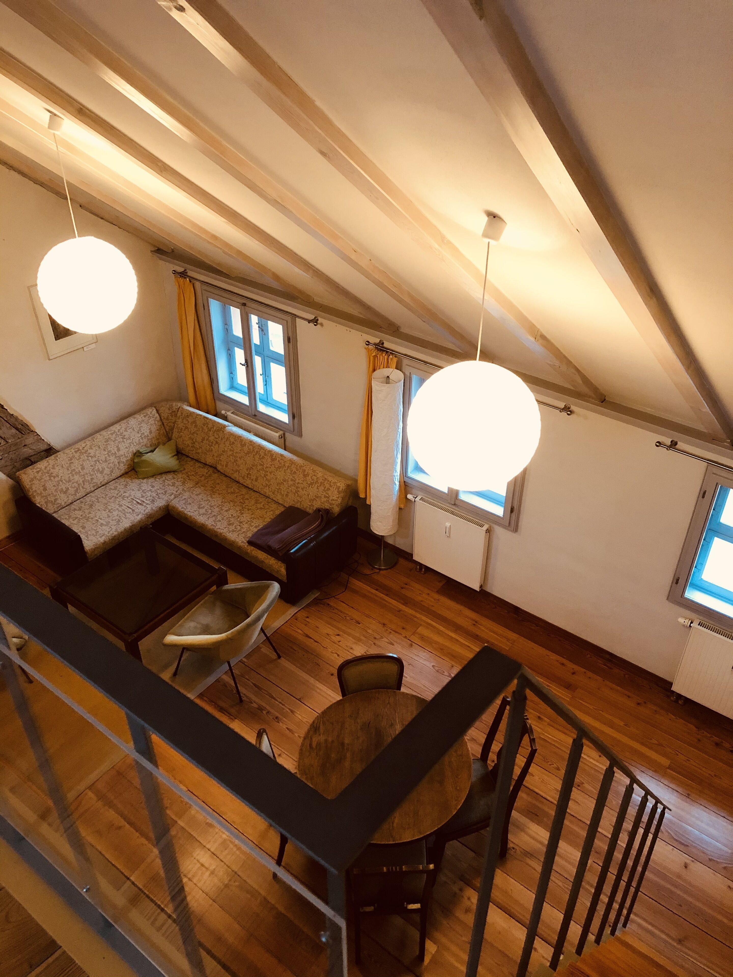 A loft-style room with a wooden floor, a sofa, a dining table, and a staircase.