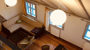 A loft-style room with a wooden floor, a sofa, a dining table, and a staircase.