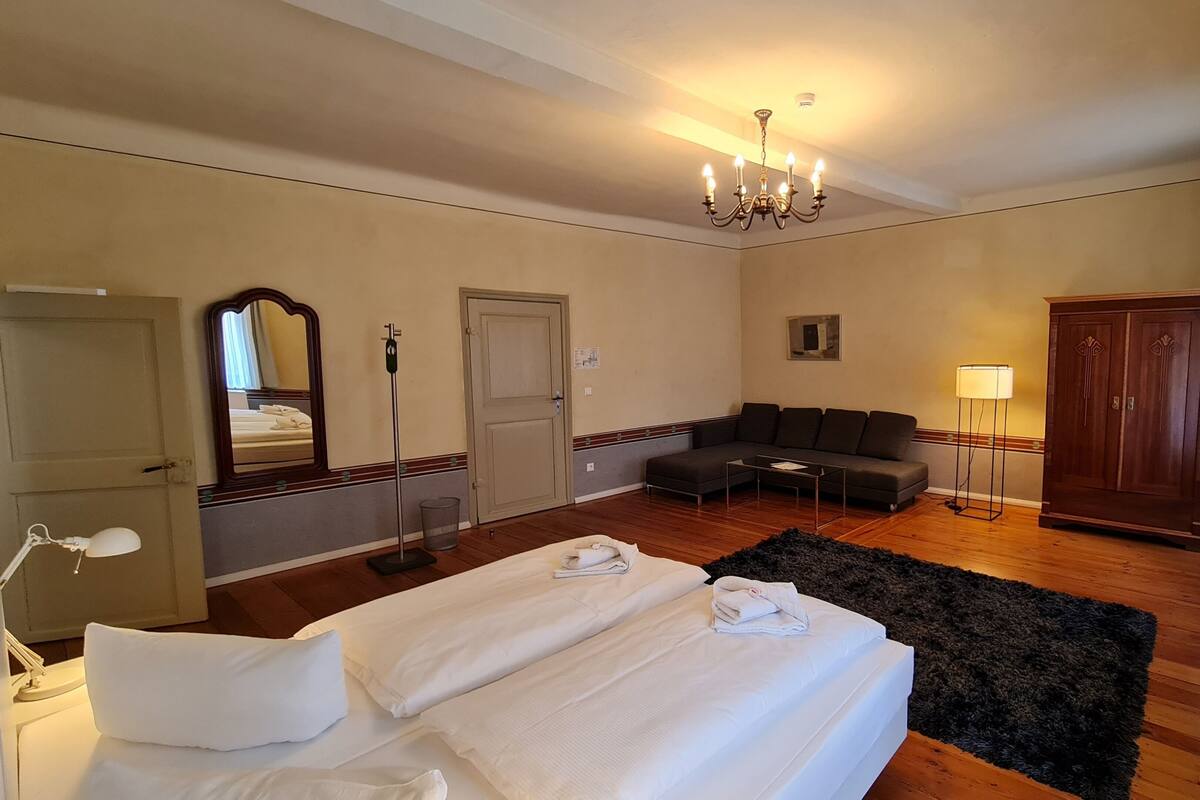 Een hotelkamer met een tweepersoonsbed, een slaapbank, een bureau, een kledingkast, een spiegel en een kroonluchter.