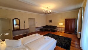 Et hotelværelse med dobbeltseng, sofa, skrivebord, garderobe, spejl og en lysekrone.