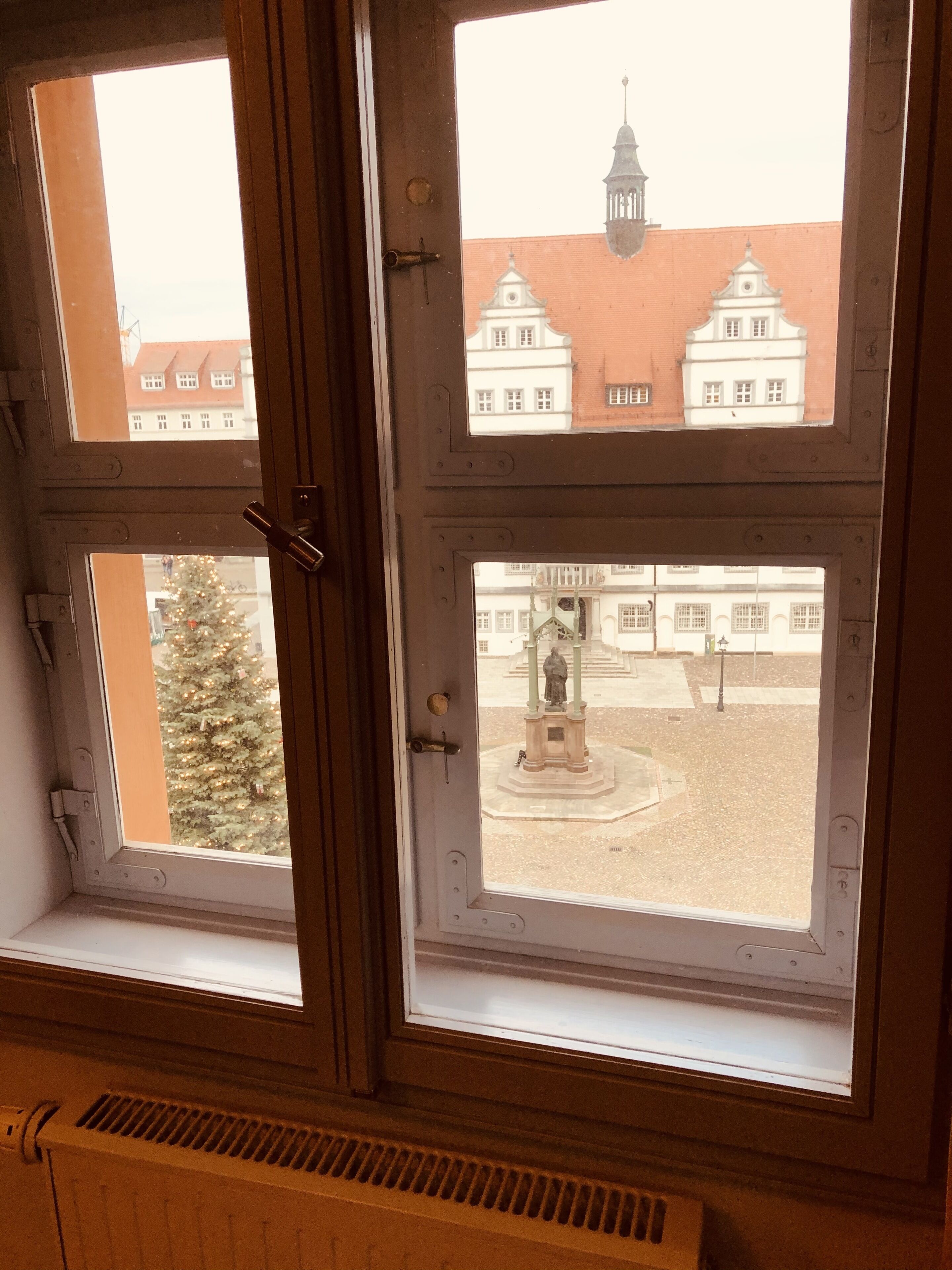 Una ventana con vistas a un patio que presenta una estatua y un edificio con techo rojo.