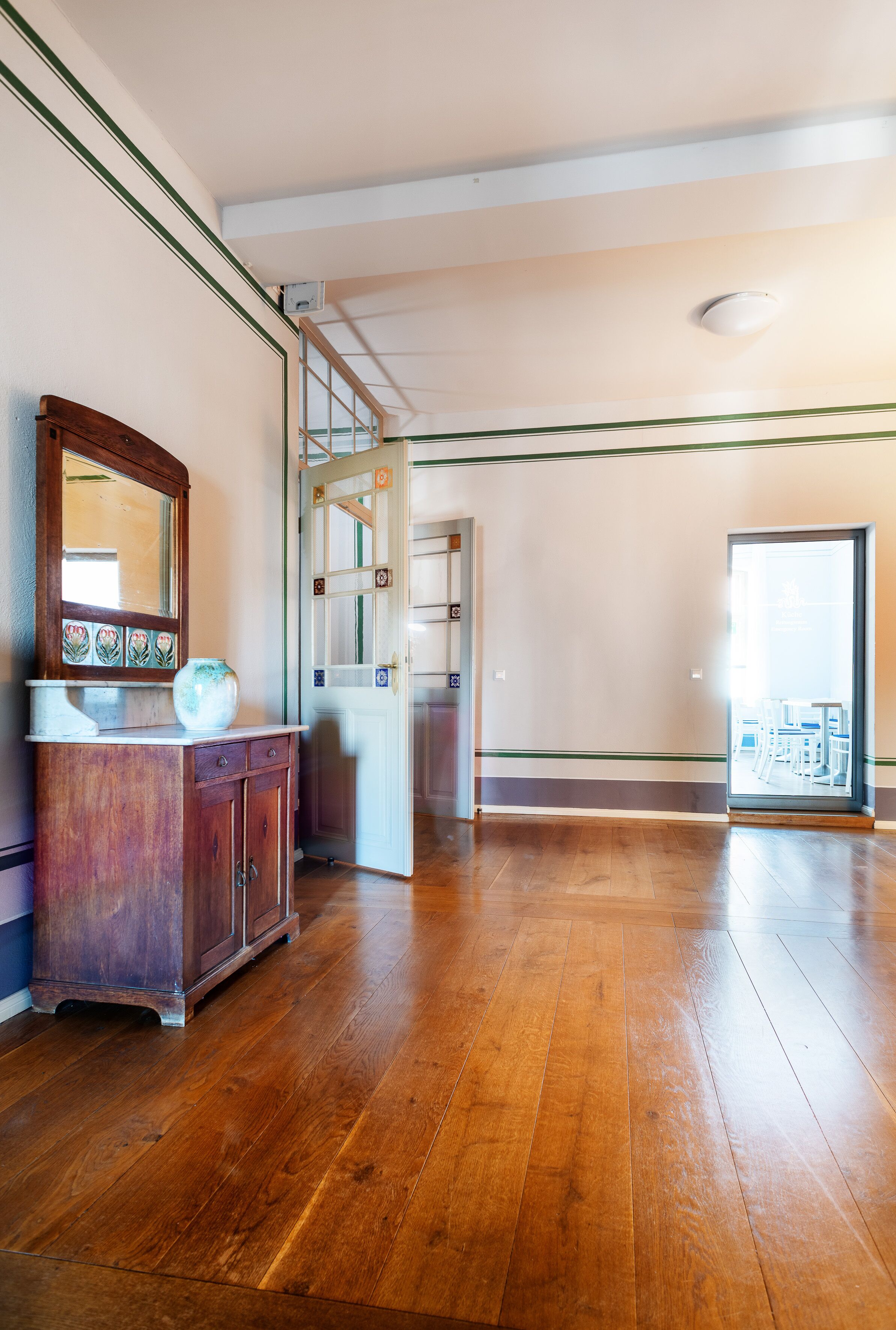Une pièce spacieuse avec un plancher en bois, une armoire en bois dotée d’un miroir et une porte donnant accès à un autre espace.