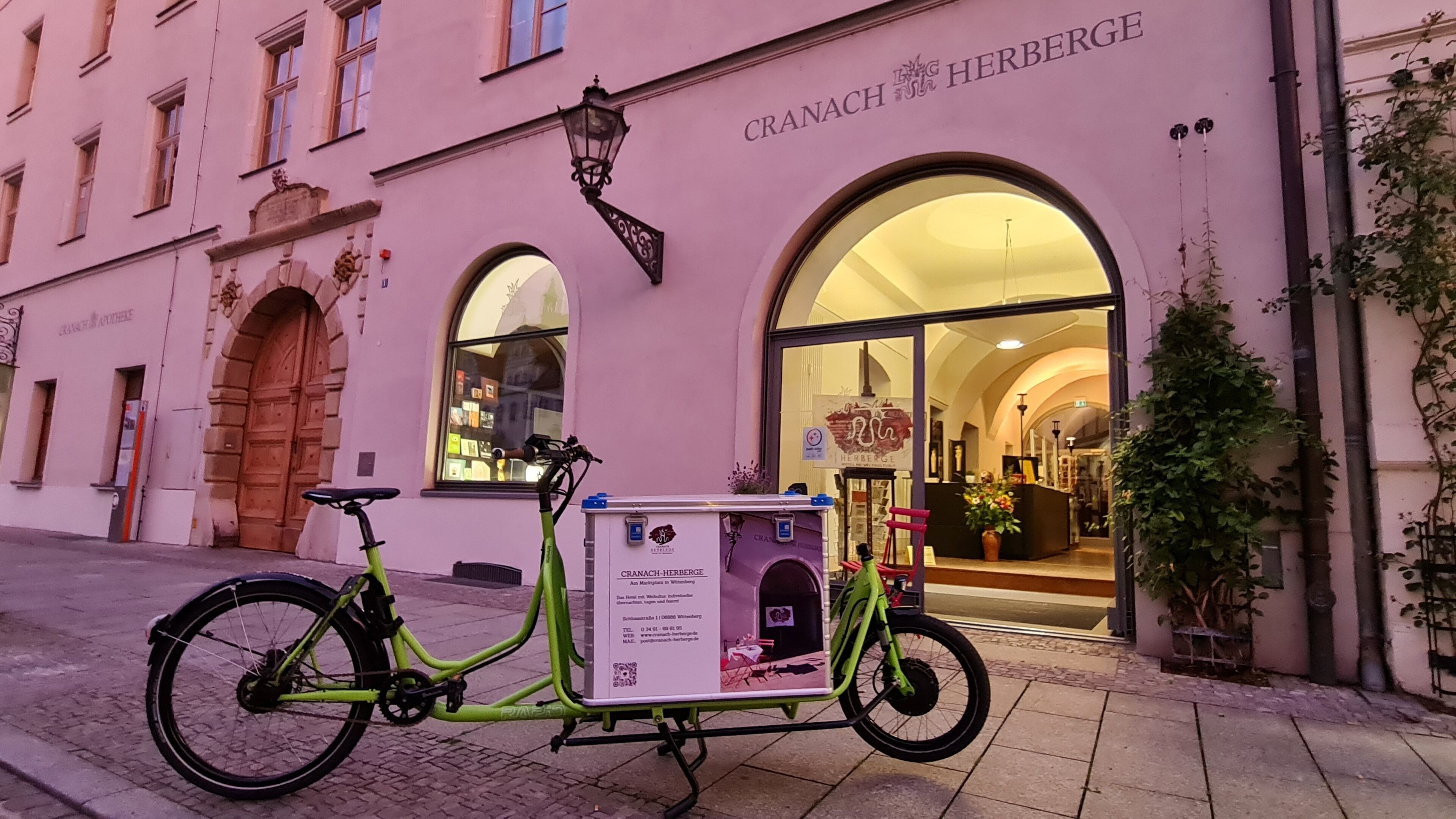 A bicycle parked in front of a building with a sign reading "CRANACH HERBERGE".