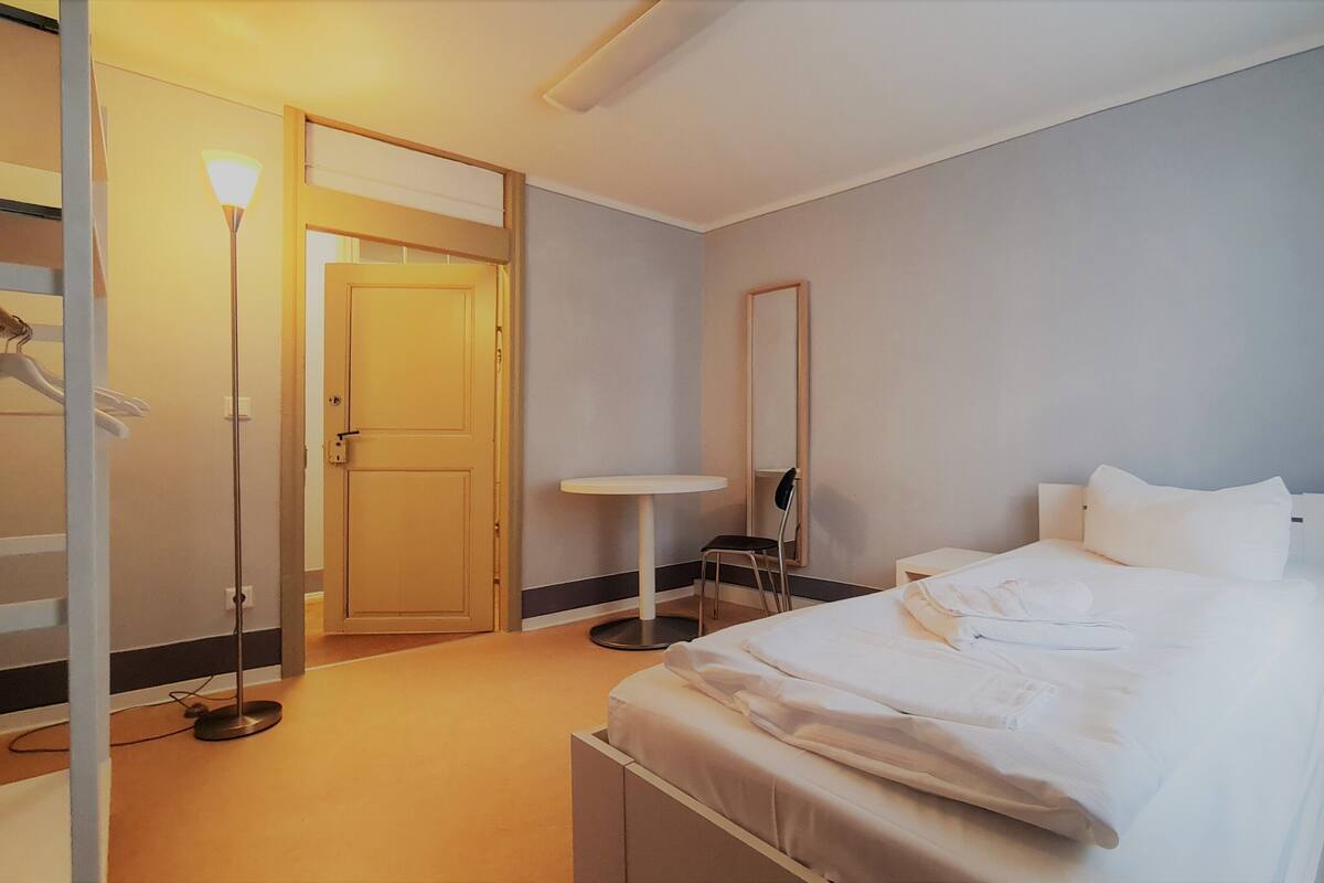 Een hotelkamer met een bed, nachtkastje, stoel, spiegel en een deur.