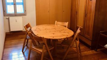 A room with a wooden dining table and chairs, a wooden wardrobe, and a window with blinds.