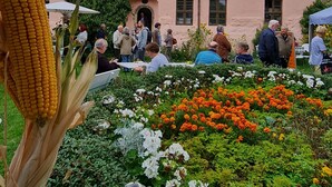 Ein Gebäude mit rosafarbenem Mauerwerk und einem Ziegeldach, umgeben von einem Garten mit verschiedenen Pflanzen und Blumen.