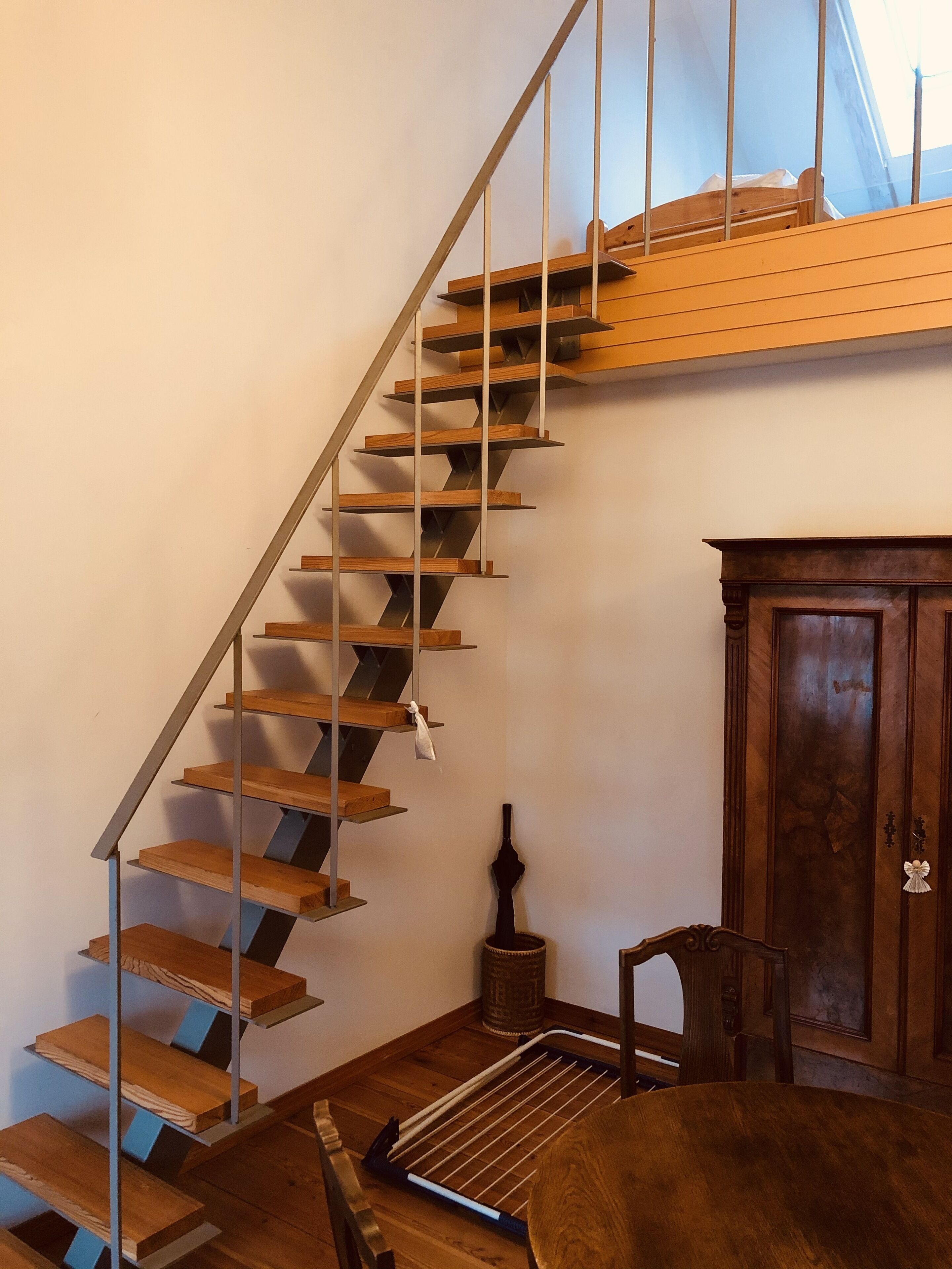 Eine Holztreppe mit Metallgeländern, eine Holztür und ein kleiner Tisch mit einem Stuhl.