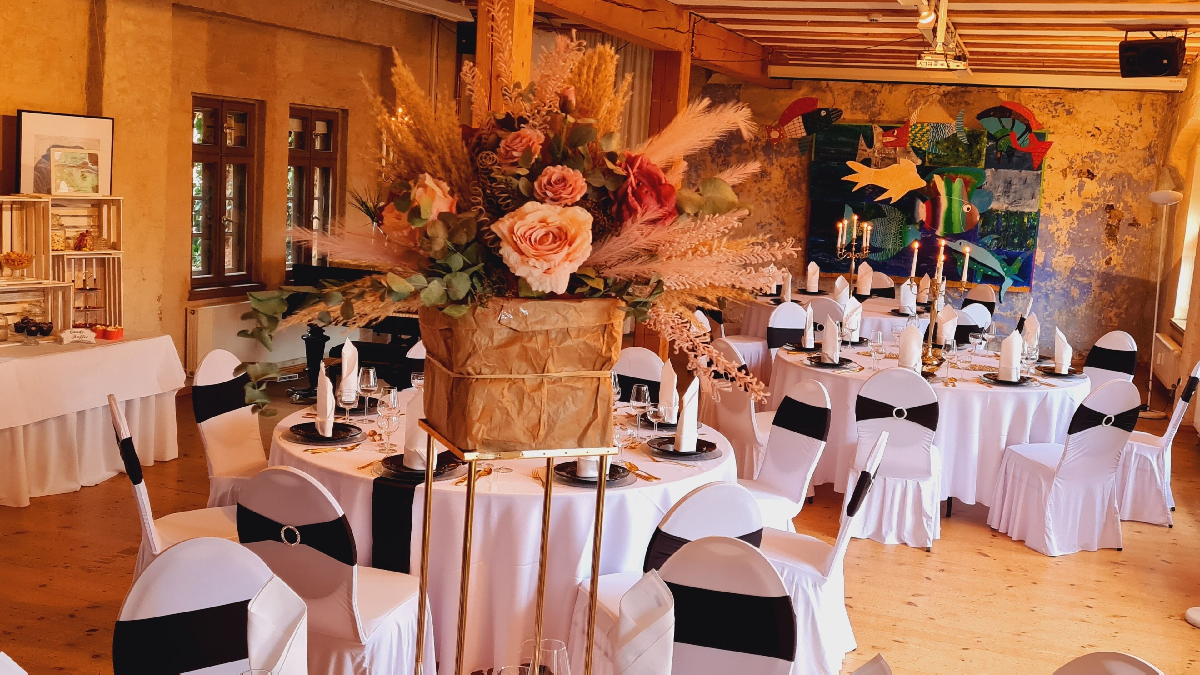 A banquet hall with round tables set for a formal event, featuring white tablecloths, black chair sashes, and floral centerpieces.
