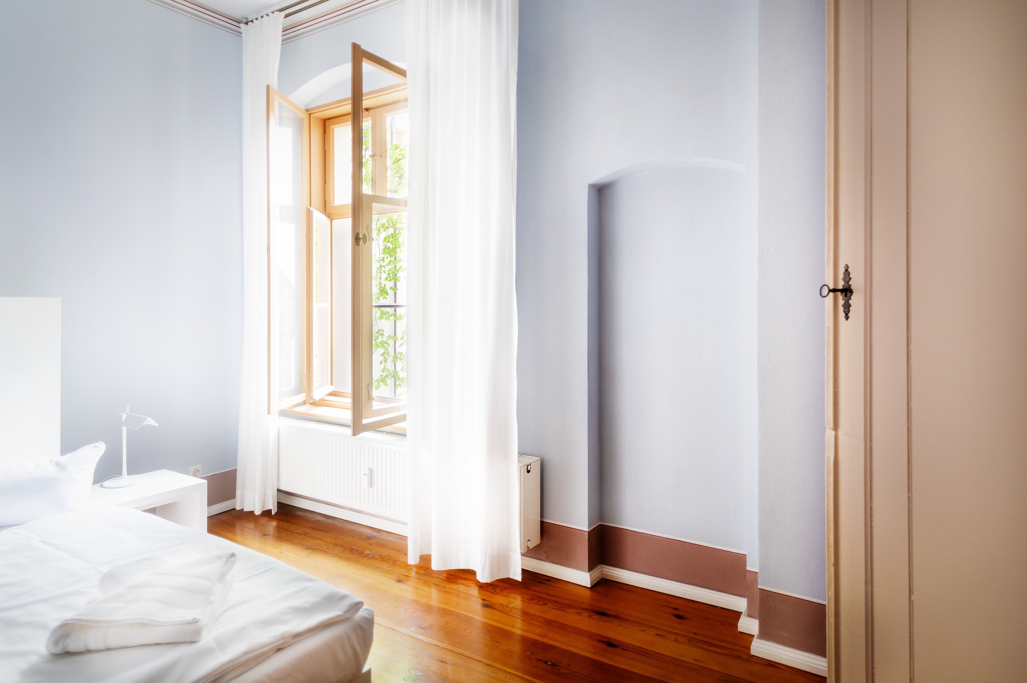 Ein Schlafzimmer mit großem Fenster, einem Bett, einem Nachttisch und einer Heizung.
