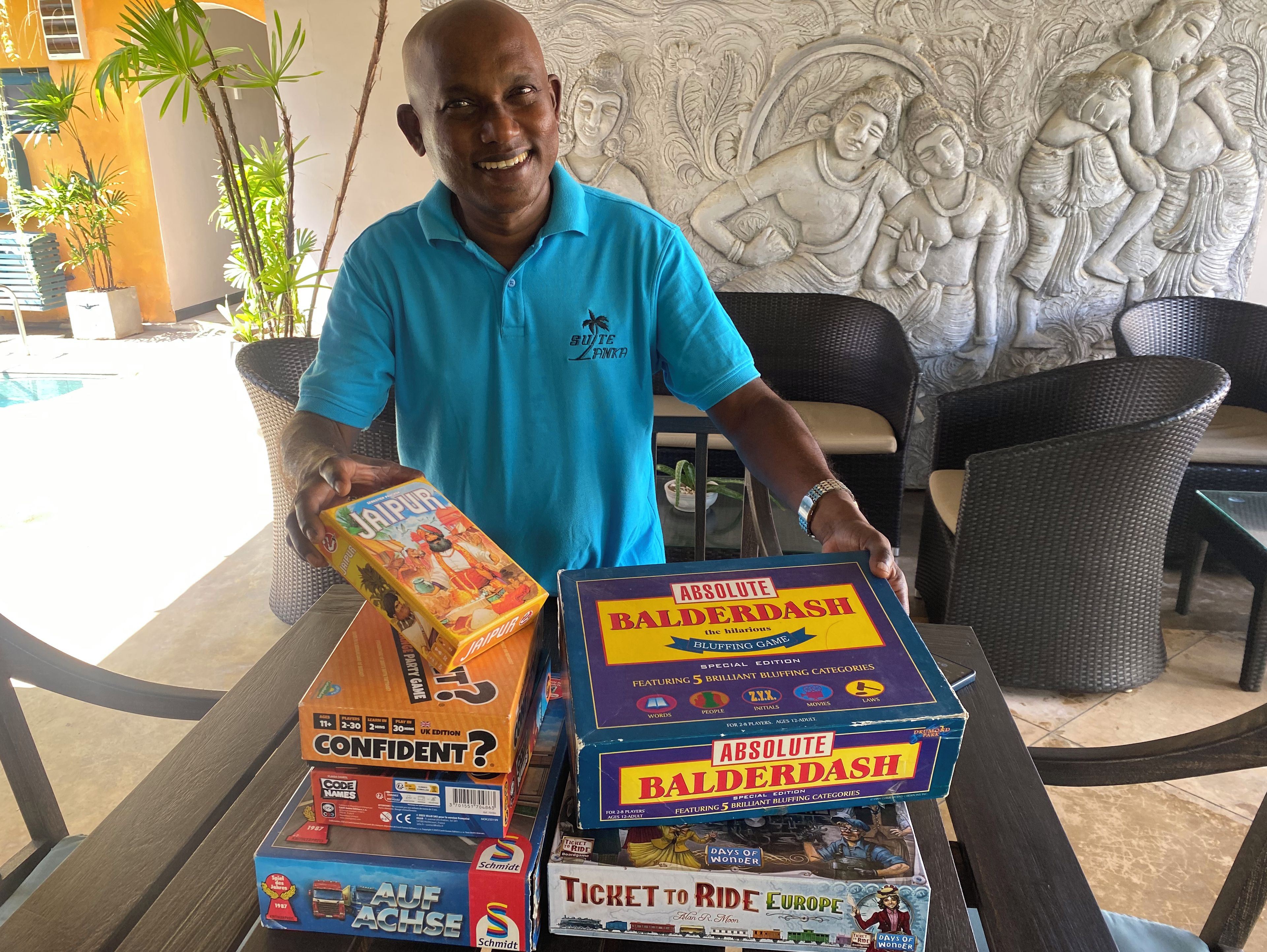 A man holding game boxes with a pool and a decorative wall in the background.