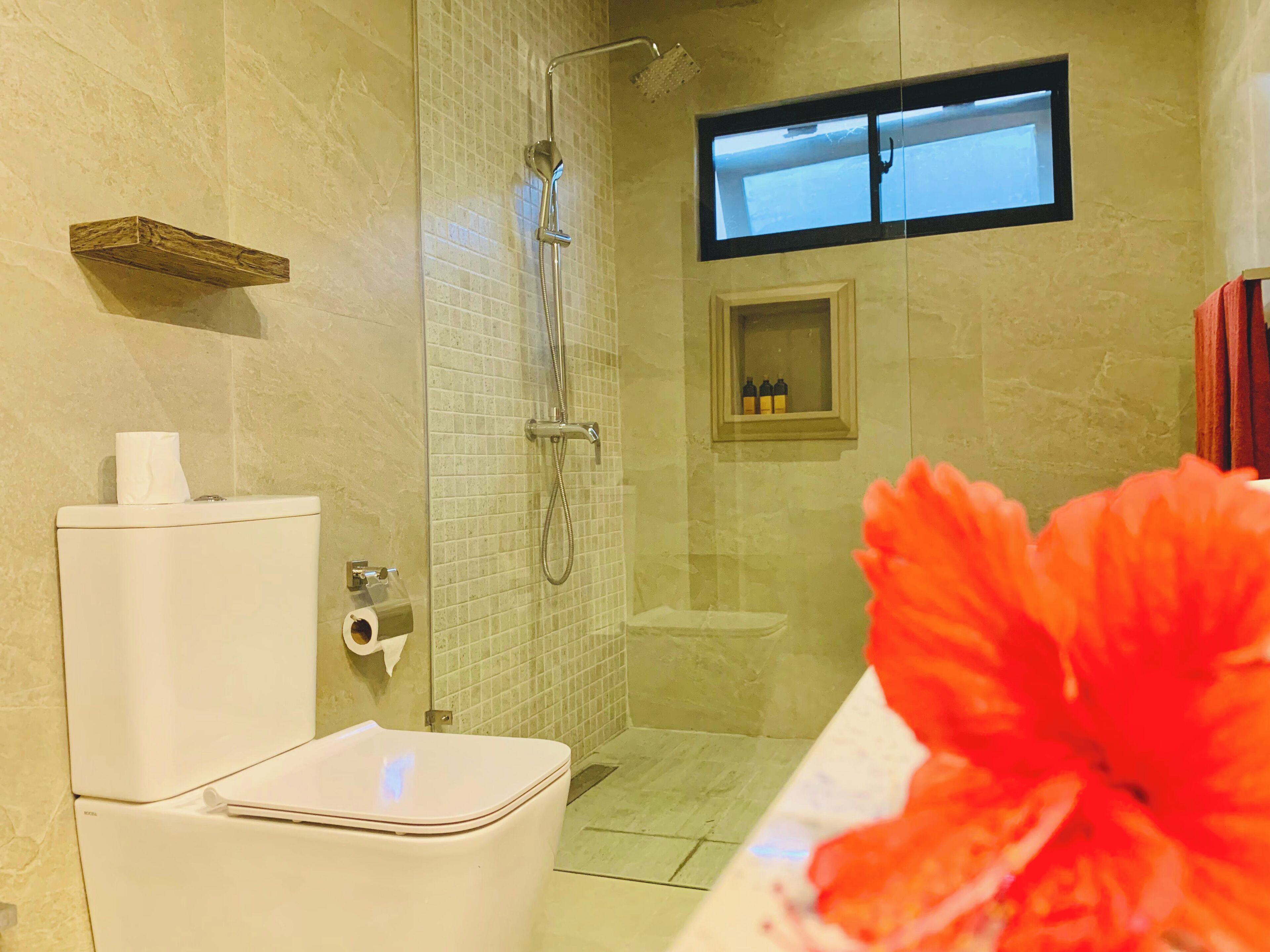 Un baño con ducha, inodoro y un ventanal pequeño.