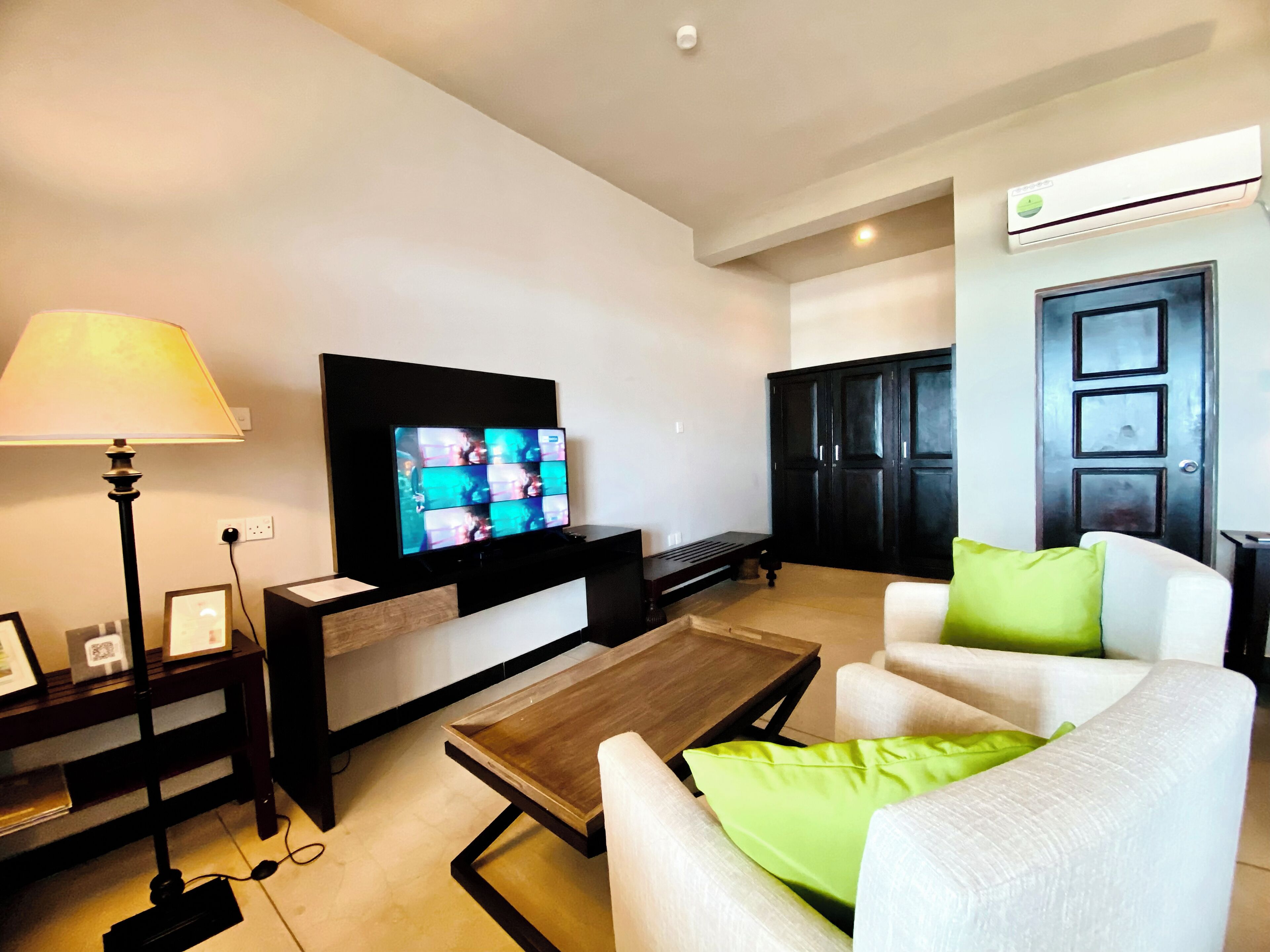 Una sala de estar con televisor de pantalla plana, lámpara, mesa de centro y sofá con un cojín verde.
