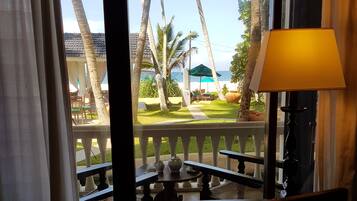 A room with a view of a beach, a table with a book, and a lamp.