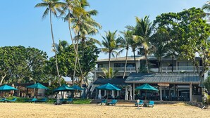 A beachfront hotel with multiple levels, palm trees, and beach chairs. - Suite Lanka (Hikkaduwa)