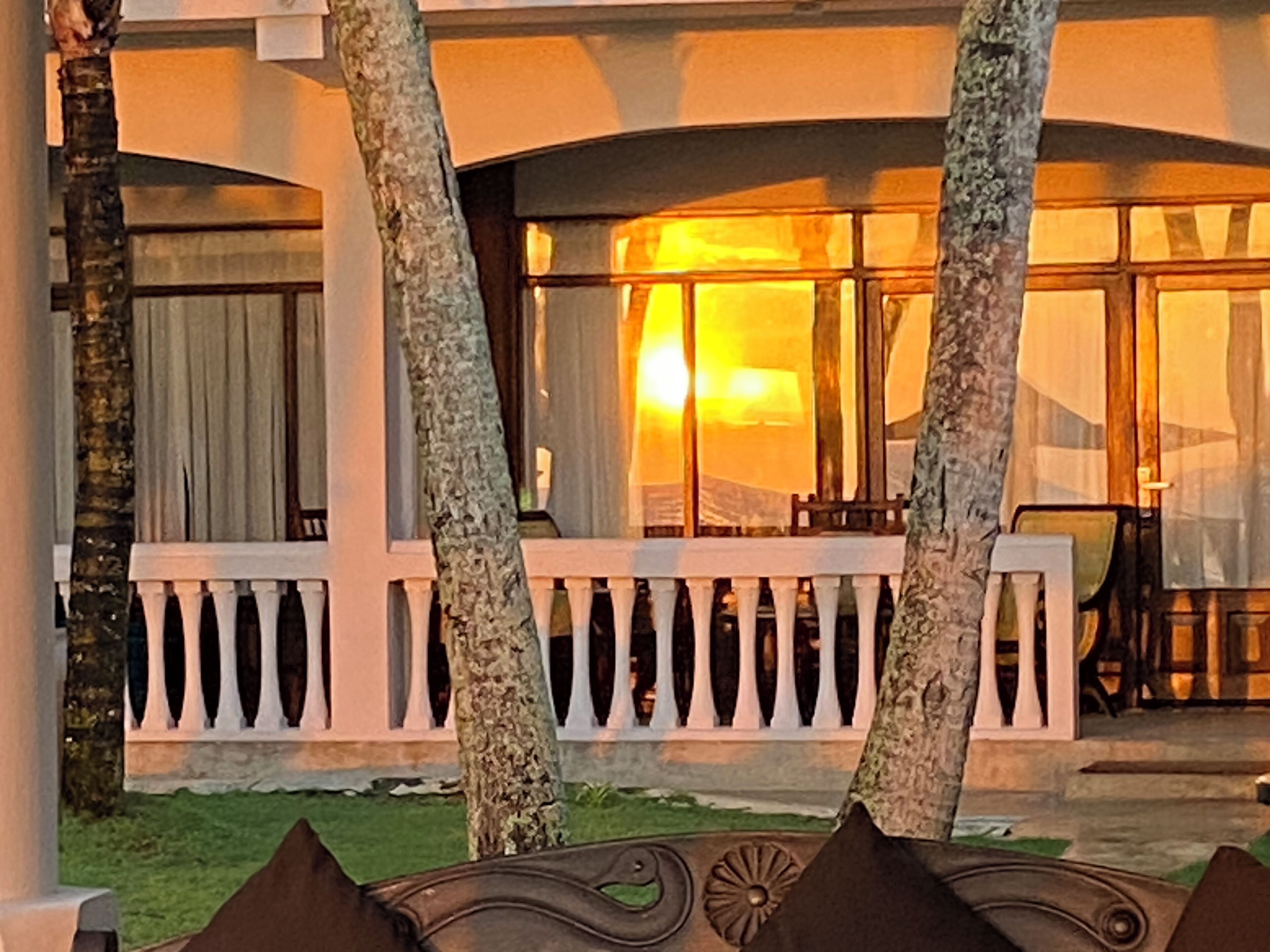 Exterior de un hotel con balcón blanco, palmeras y vista al atardecer.