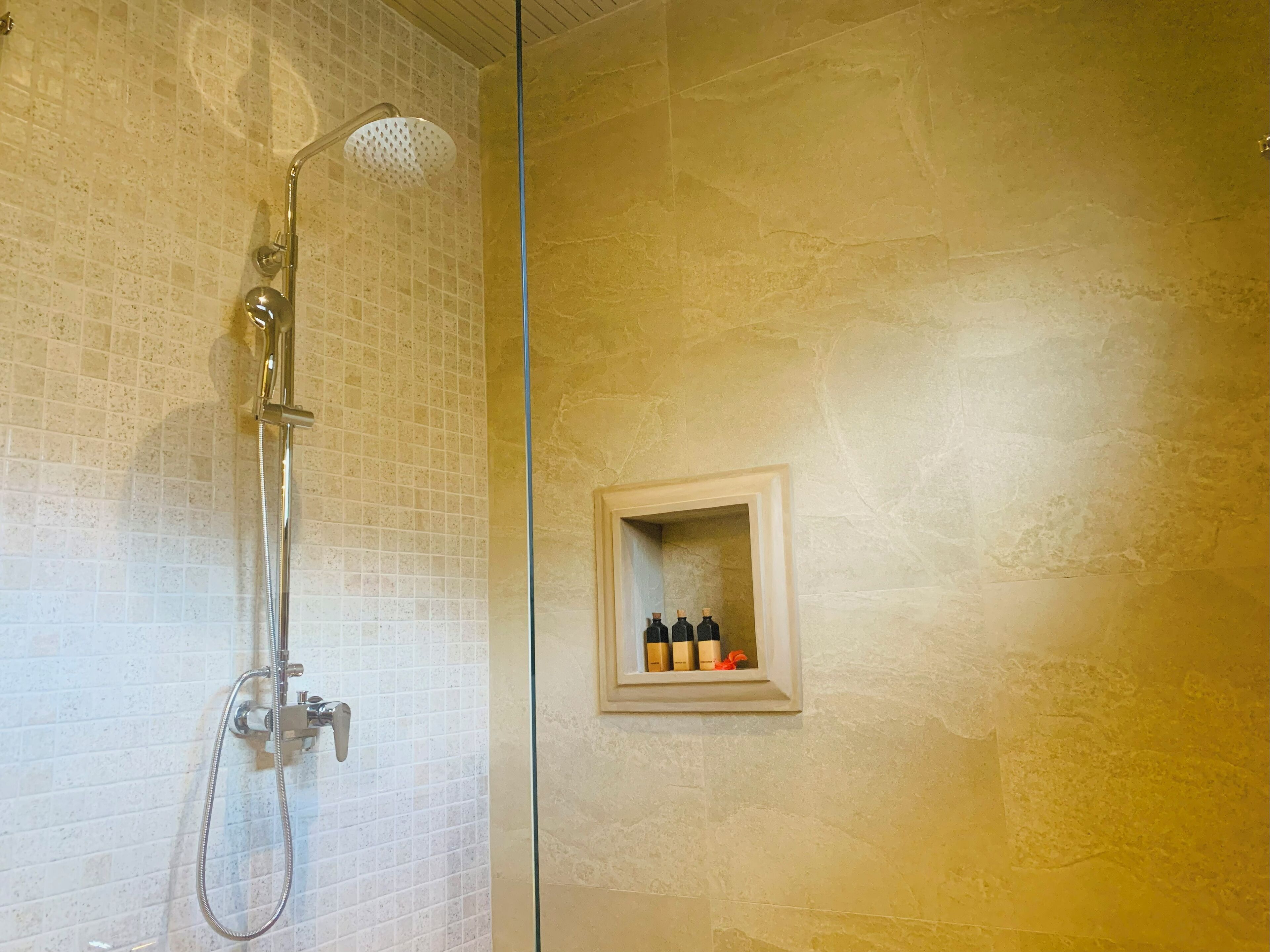 A bathroom with a shower, tiled walls, and a shelf with bottles.