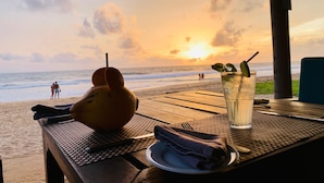 A table with a glass of iced drink, a wrapped napkin, and a fruit on the table. - Suite Lanka (Hikkaduwa)