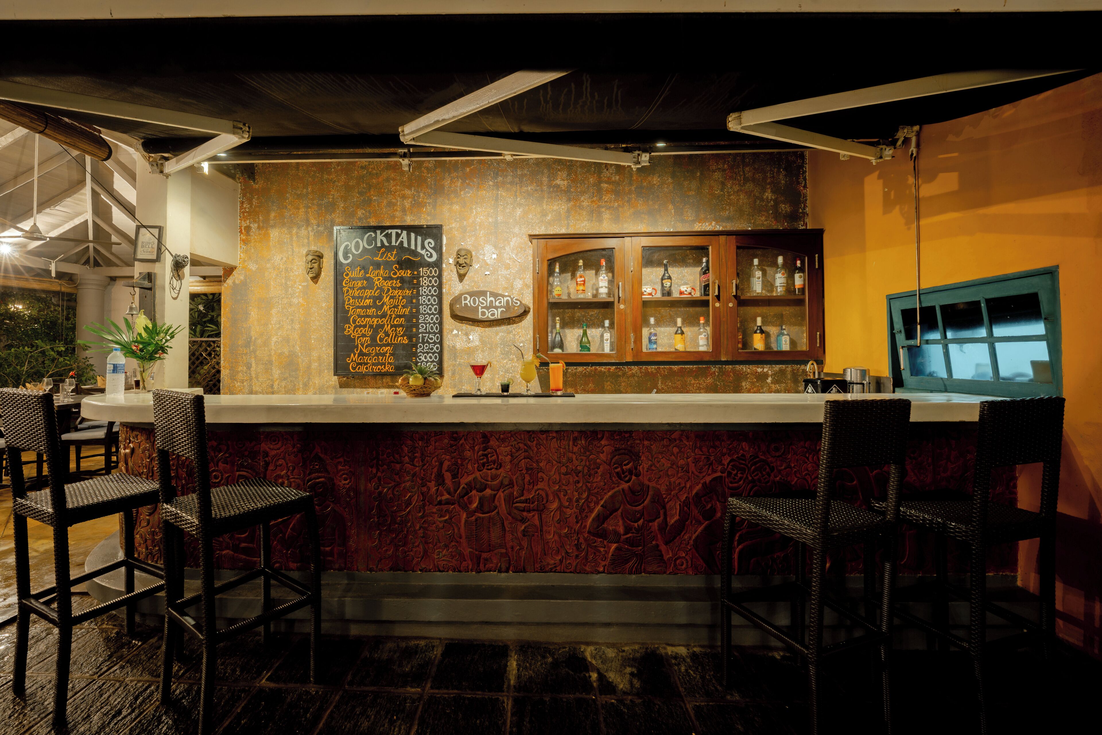 A bar area with a cocktail menu, bar stools, and a cabinet with bottles.