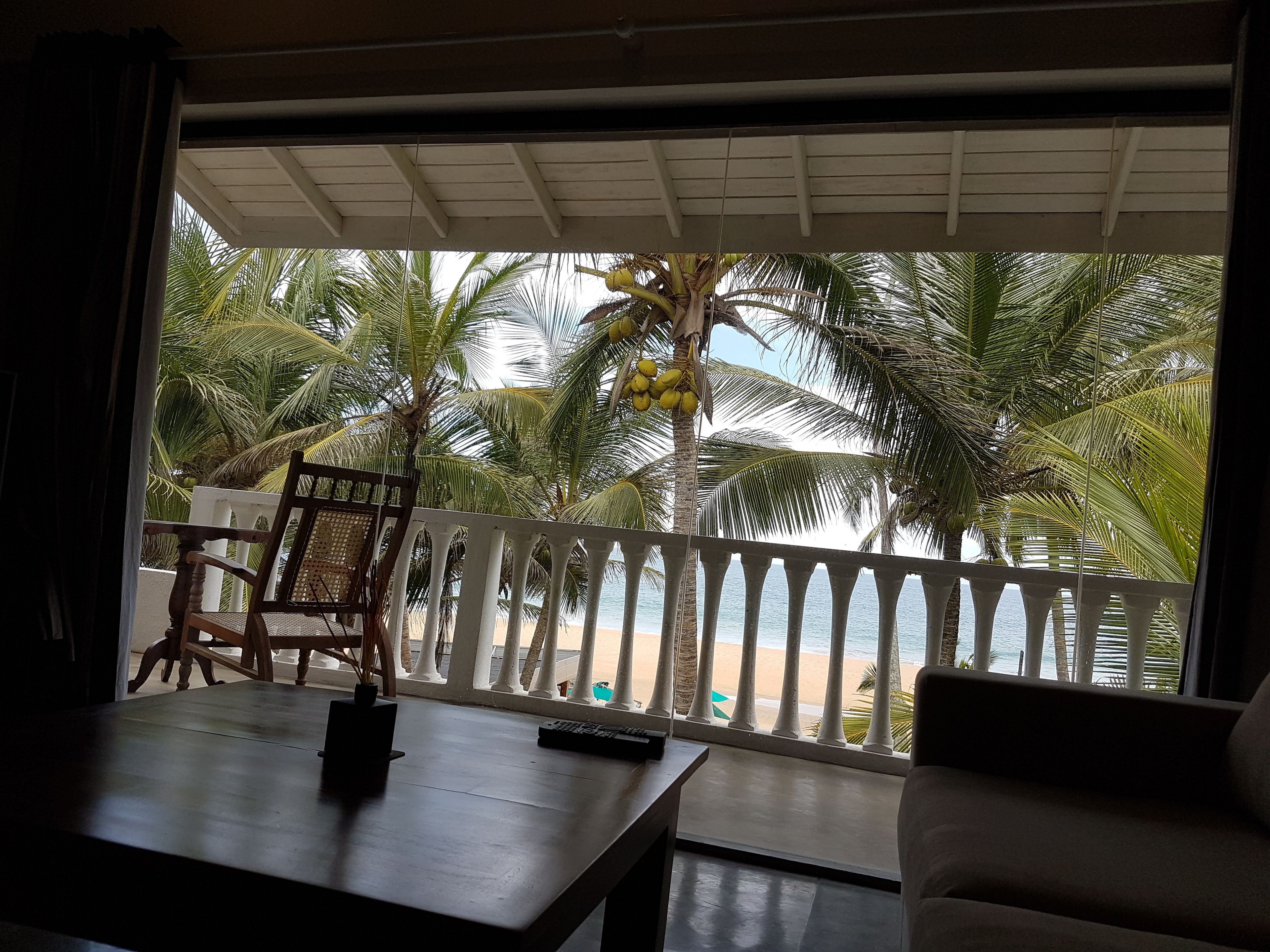 A room with a balcony overlooking a beach, featuring a table, a chair, and a sofa.