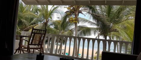 A room with a balcony overlooking a beach, featuring a table, a chair, and a sofa.