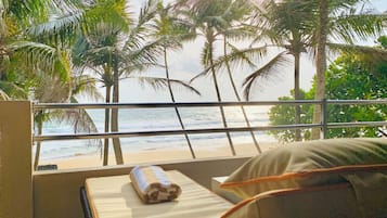 Enjoy a serene beach view from the comfort of your room, featuring a plush bed and a window overlooking the ocean.