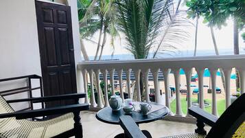 A balcony with a view of the beach, featuring a table with cups and a chair.