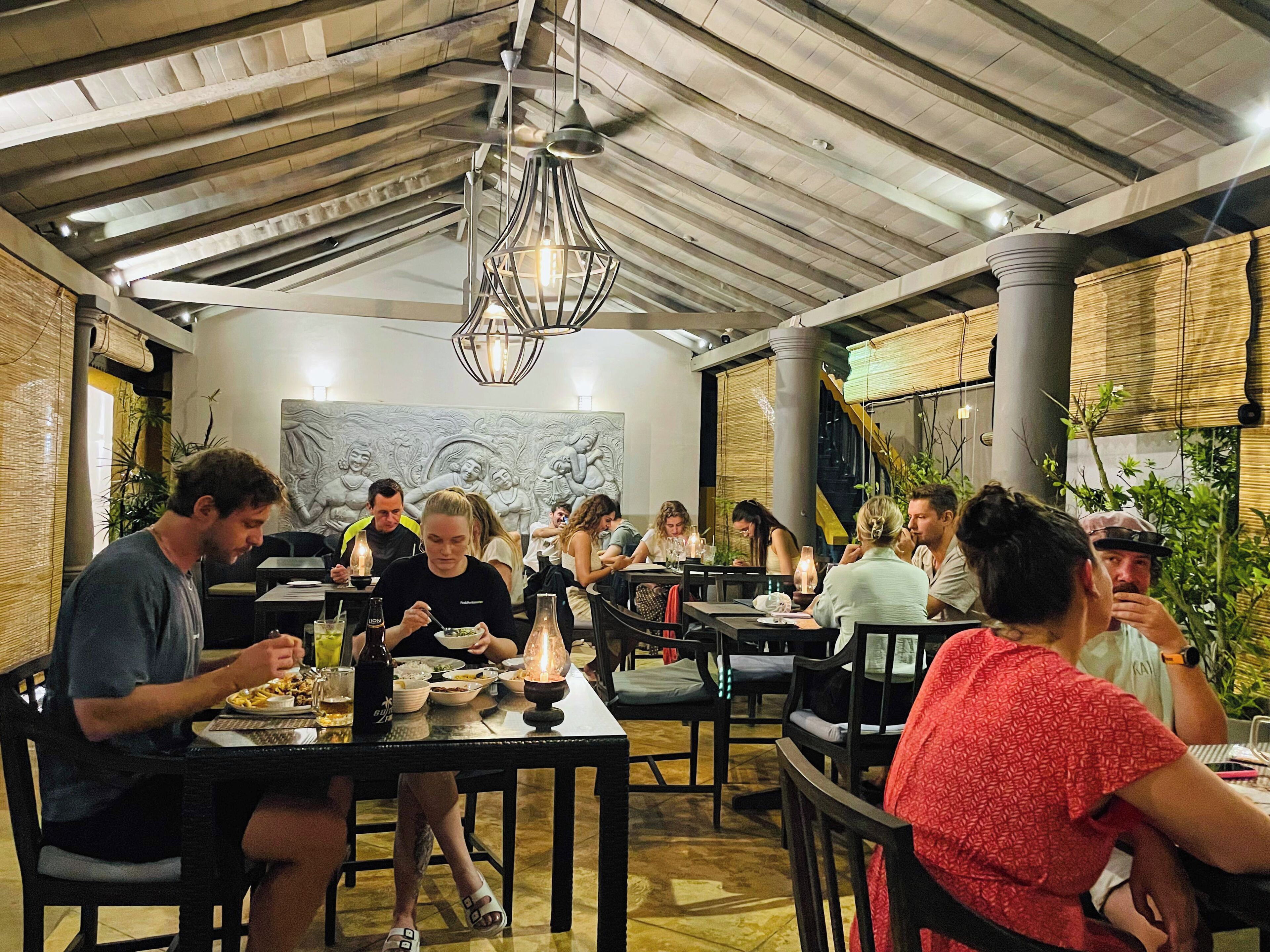 Un restaurante con techos altos, vigas a la vista y una decoración rústica. Las mesas están dispuestas para comer y los comensales están sentados.