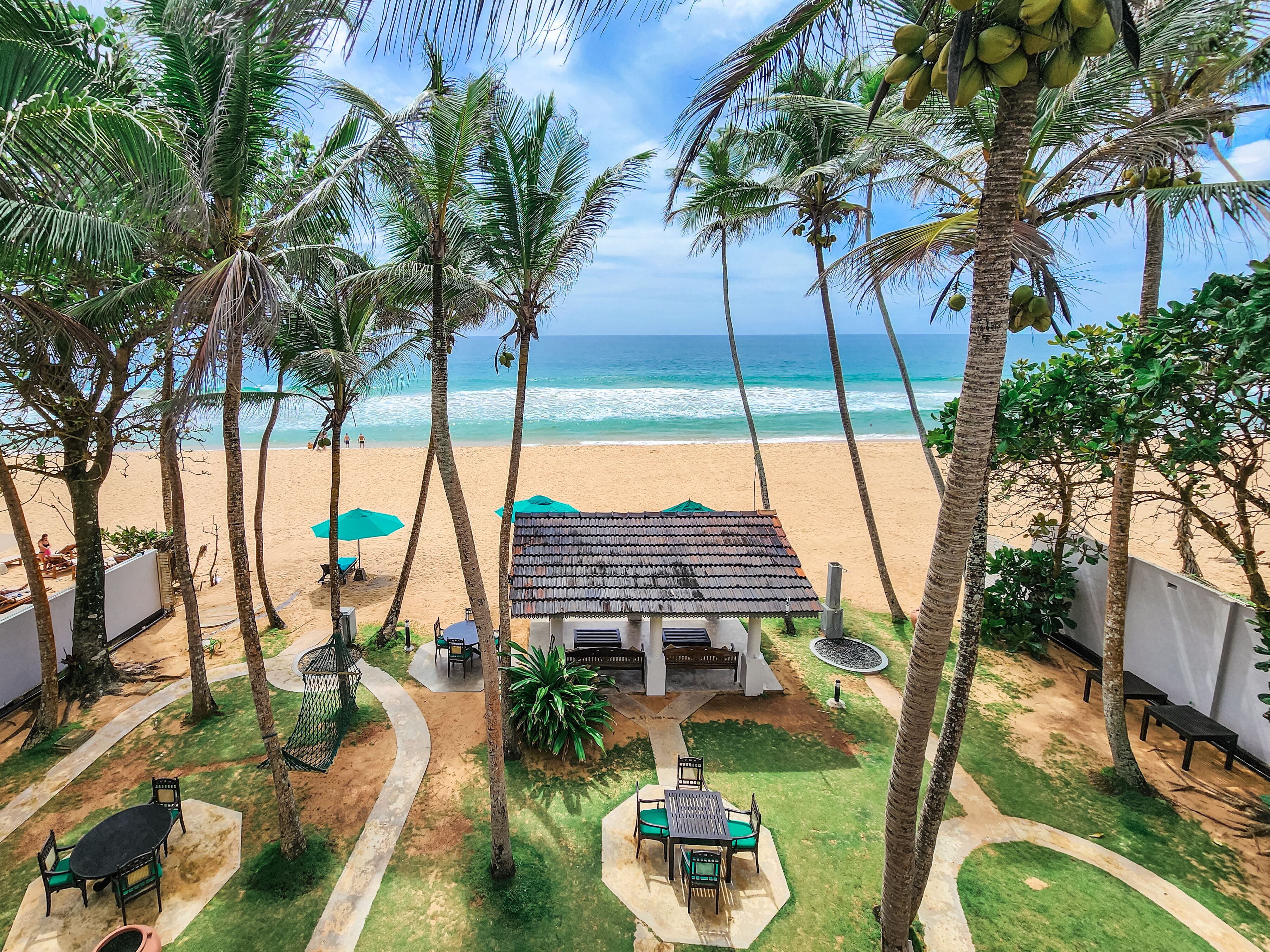 A beach view with palm trees, a small hut, and outdoor seating.