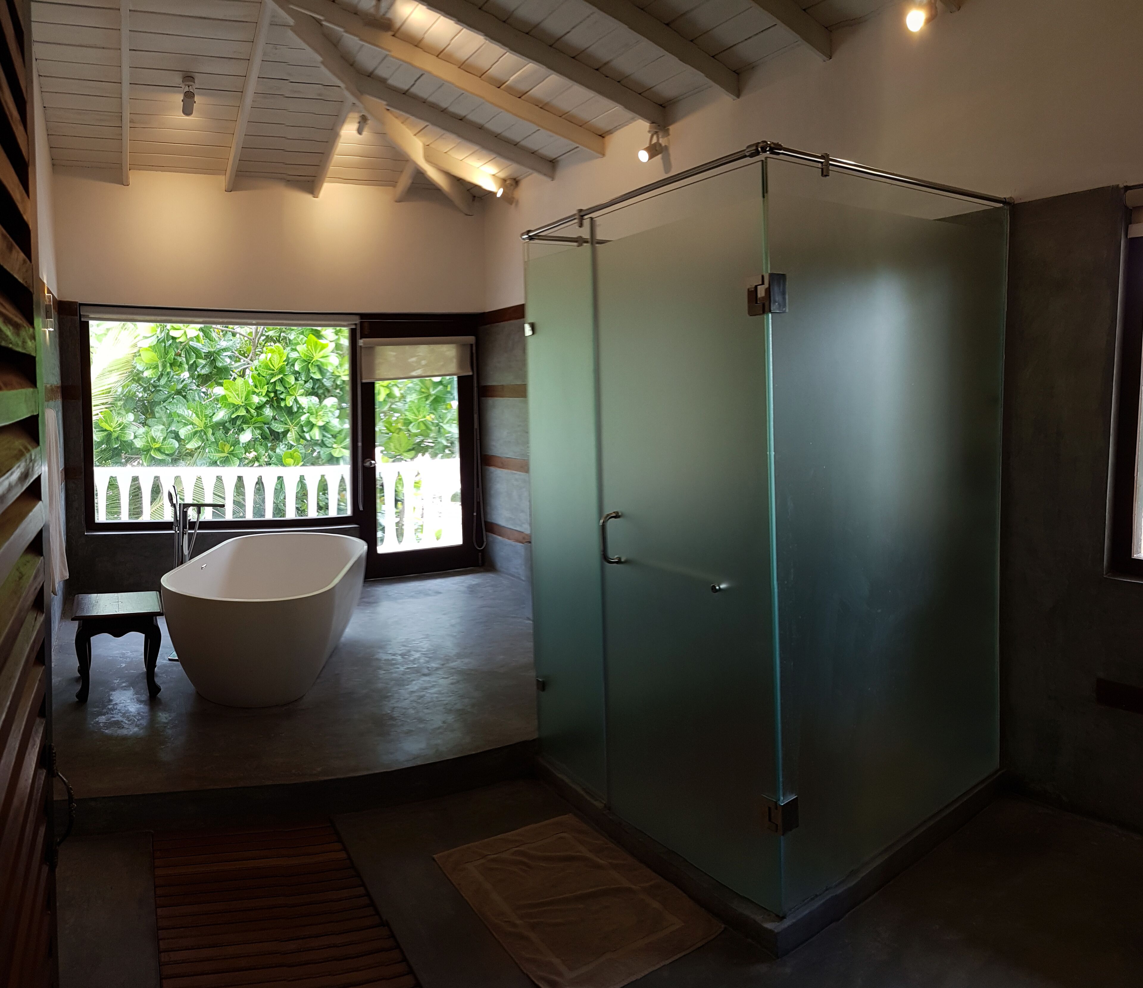 Un baño moderno con una bañera independiente, ducha con mampara de vidrio y vistas a zonas verdes exteriores.