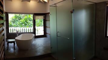 Un baño moderno con una bañera independiente, ducha con mampara de vidrio y vistas a zonas verdes exteriores.