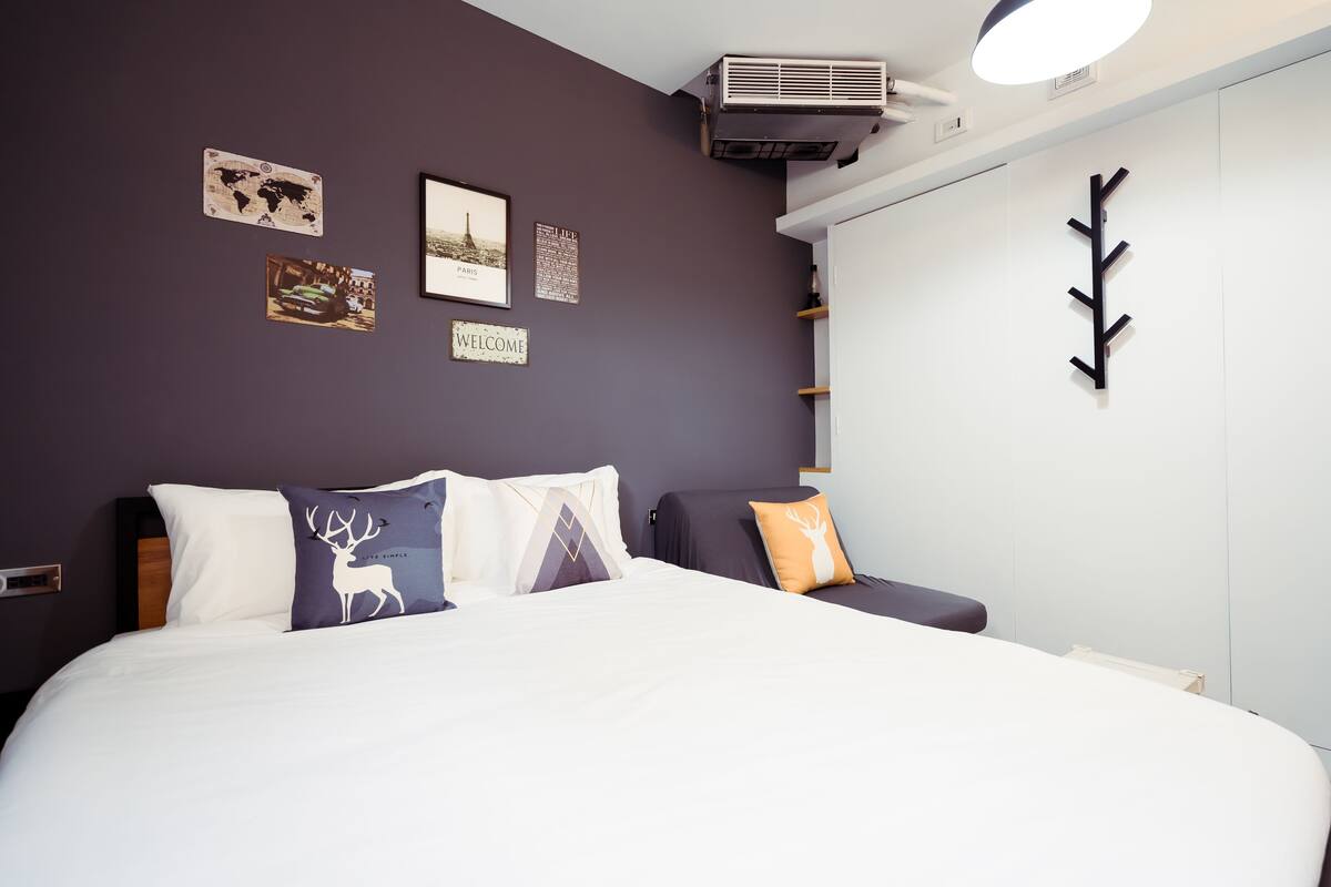 Quarto de hotel moderno com cama grande, mesa de cabeceira, ar condicionado fixado na parede e mapa mundi decorativo.