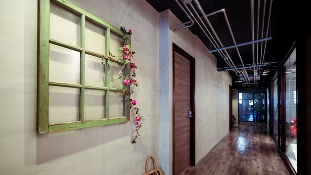 Un couloir avec un plancher en bois, une fenêtre à cadre vert et une porte.