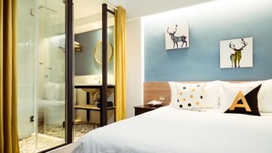 Une chambre d’hôtel dotée d’une douche en verre, d’un lit avec une literie blanche et de deux œuvres d’art représentant des cerfs, accrochées au mur.