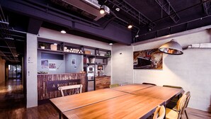 Une salle de conférence moderne, dotée d’une longue table en bois, de chaises, d’un coin cuisine et d’une lampe fixée au mur.