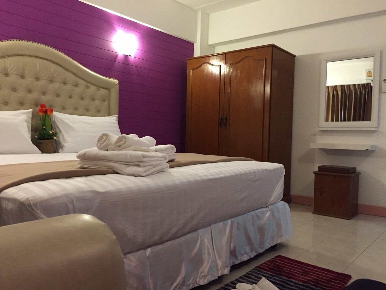 A hotel room with a bed, a wooden wardrobe, a small table, and a window with curtains.