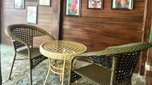 Une pièce avec des chaises en osier et une table ronde, des murs en bois et des peintures abstraites aux couleurs vives.