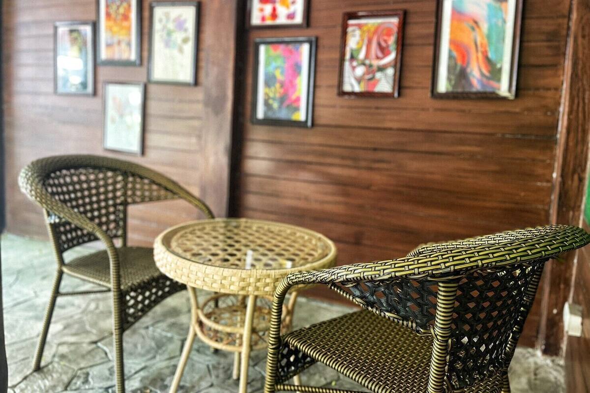 A room with wicker chairs and a round table, wooden walls, and colorful abstract paintings.