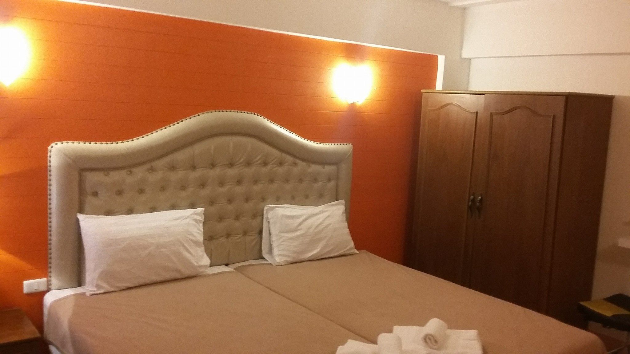 Habitación de hotel con una cama grande, dos almohadas, un armario de madera y una lámpara fijada a la pared.