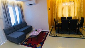 A living room with a sofa, a small table with a floral table runner, and a dining area with a chandelier and curtains. - Brew Home (Bacolod)