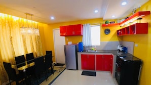A compact kitchen with red cabinets, a refrigerator, a sink, and a dining area with a table and chairs. - Brew Home (Bacolod)