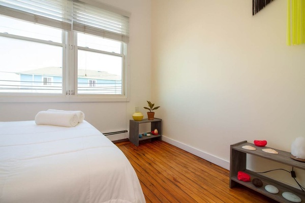 Bright, minimalist bedroom with hardwood floors, cozy bed, and sunny windows—clean, calm, and thoughtfully styled.