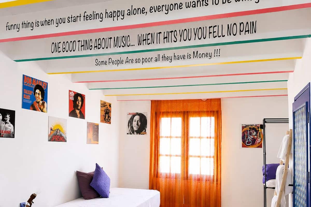 A room with two beds, a window with curtains, and various posters on the walls.