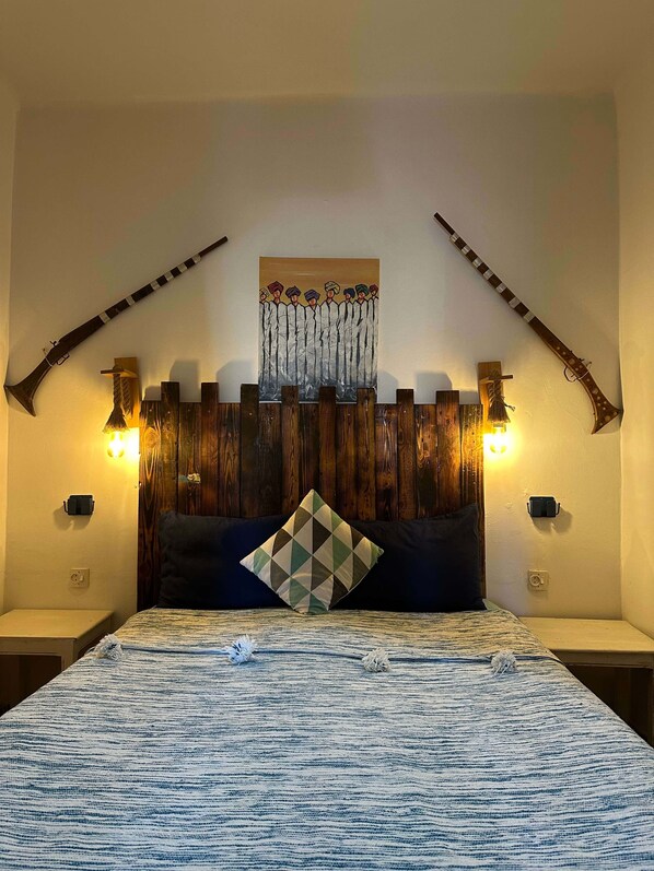A bedroom with a bed, a wooden headboard, two wall-mounted lights, and two decorative axes. - Yousurf Surf House (Essaouira)
