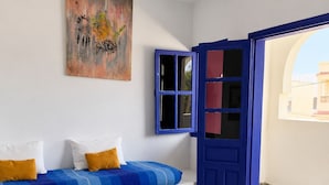 A room with a blue sofa, a small table, a colorful rug, a blue door, and a painting on the wall. - Yousurf Surf House (Essaouira)
