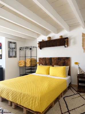 A bedroom with a wooden bed frame, a yellow quilted bedspread, and a headboard with a wooden panel. - Yousurf Surf House (Essaouira)