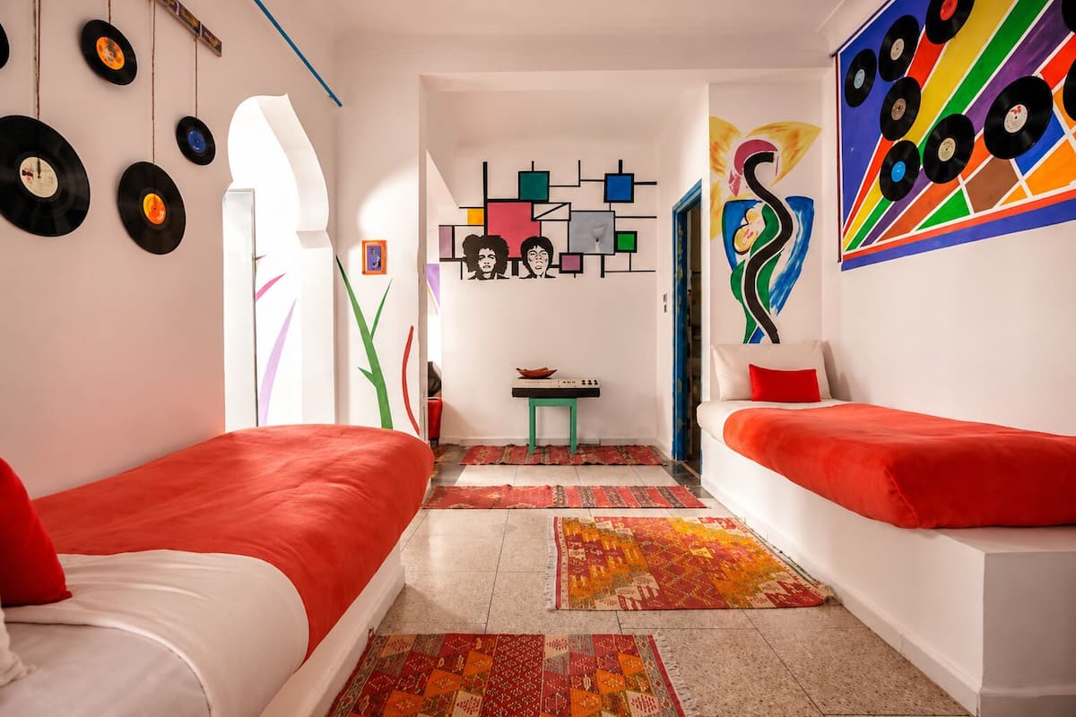 A room with two beds, a small table, and a colorful abstract painting on the wall.