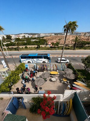 A bus parked at a bus station with people waiting, surrounded by surfboards and umbrellas. - Yousurf Surf House (Essaouira)
