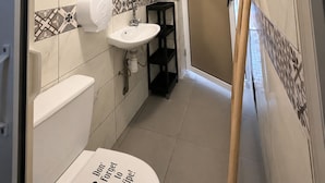 A narrow bathroom with a toilet, sink, and mirror. - Yousurf Surf House (Essaouira)