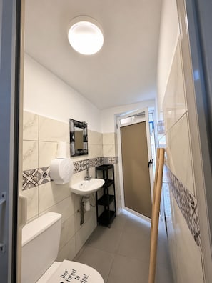 A narrow bathroom with a toilet, sink, and mirror. - Yousurf Surf House (Essaouira)