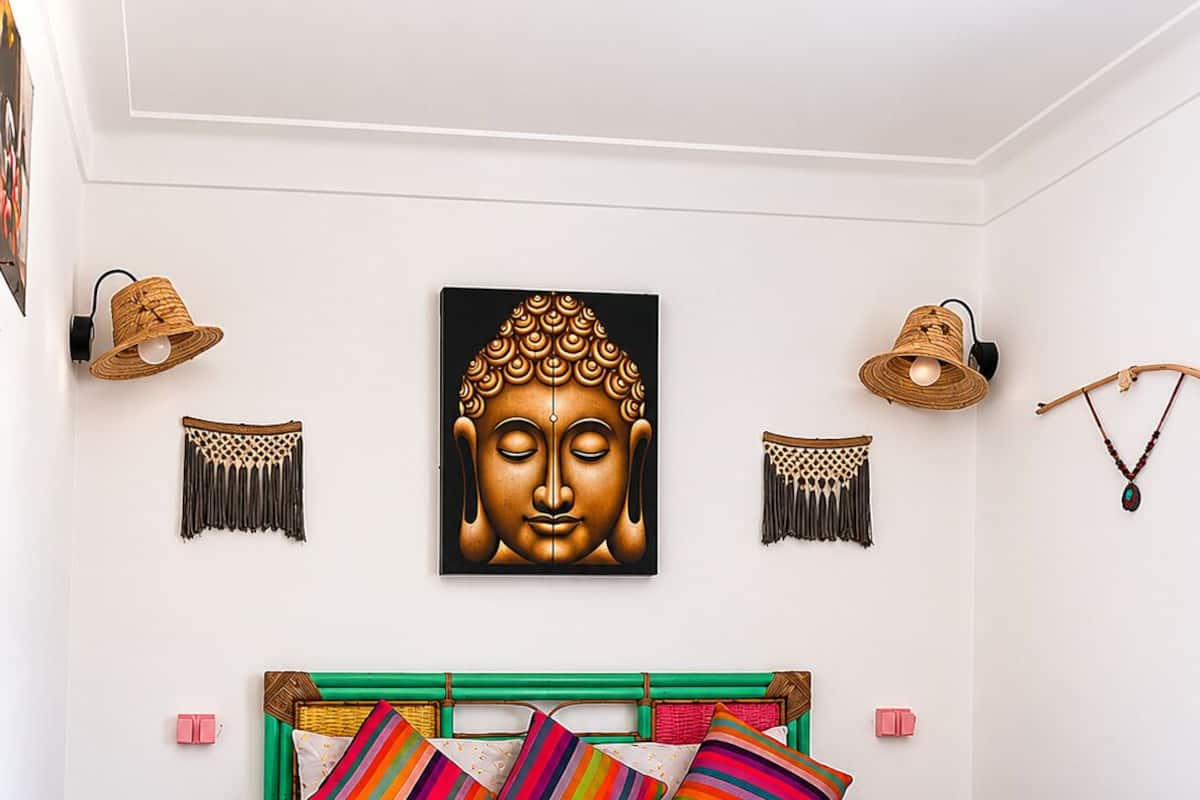 A bed with a green frame, colorful pillows, and a Buddha painting above it.